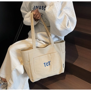 Detail view of beige canvas tote bag showing the TCT embroidery and functional side pockets