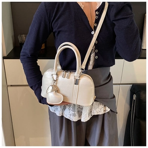 Detail view of pearl white crossbody shell bag with heart charm and adjustable strap