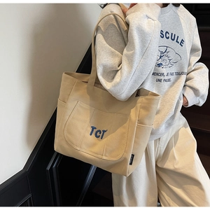 Detail of beige canvas tote bag with TCT embroidery and side pockets for commuting