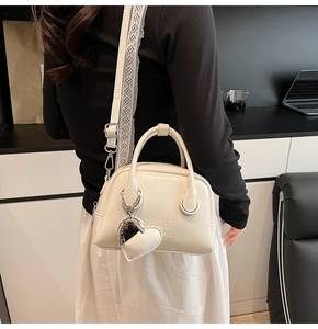 Detail of cream bowling bag with lace strap and heart charm on a black outfit
