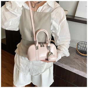 Detail of light pink shell bag with vertical embossed stripes and heart charm accessory
