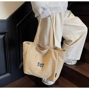 Detail of beige canvas tote bag with blue TCT embroidery and side pocket shown on stairs