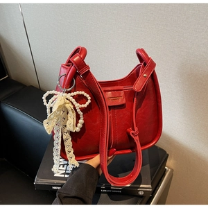 Detail of red faux leather saddle bag with pearl and lace bow charm decoration