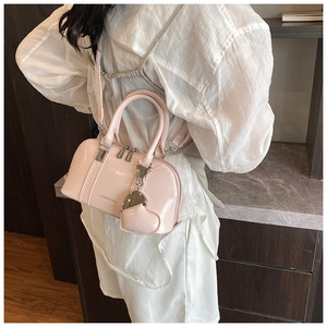 Modern pink glossy shell handbag shown on person with heart charm and shoulder strap
