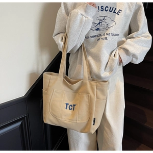Detail of beige canvas tote bag featuring navy blue TCT embroidery and thick texture