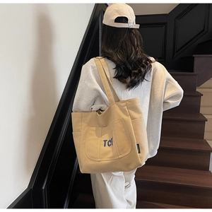 Detailed back view of a large canvas tote bag with blue TCI embroidery on stairs