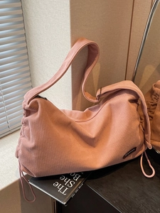 Pink corduroy tote bag with drawstring detail and round patch on a dark table