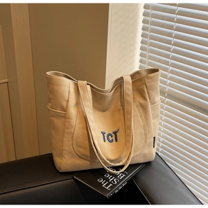 Detailed macro view of beige canvas tote bag with blue TCT embroidery on leather chair