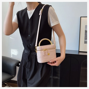 Detail of pink quilted box bag with gold floral emblem and curved metallic handle