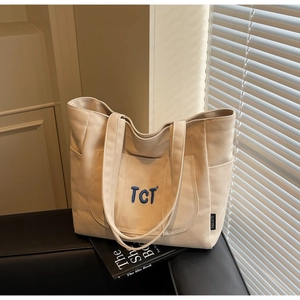 Detail of beige canvas tote bag showing TCT blue embroidery and functional side pockets