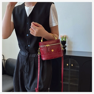 Detail of red quilted cylindrical box bag featuring gold floral logo and top handle