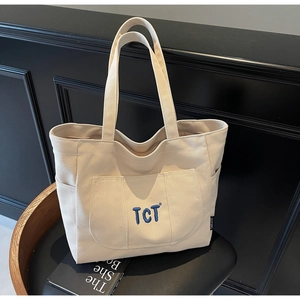 Detail view of cream canvas tote bag with TCT embroidery and side pockets on a chair