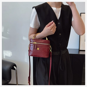 Close-up of wine red quilted box bag with gold floral clasp and curved metal handle