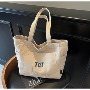 Detailed close-up of cream canvas tote bag with TCT blue embroidery and side pockets