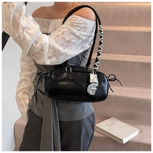 Detail of glossy black cylinder bag with double straps and metallic letter pendant