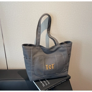 Close-up of deep grey canvas tote bag featuring orange TCT embroidery and side pockets