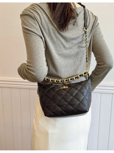 Sac à bandoulière matelassé noir avec chaîne dorée et fermoir pivotant porté par mannequin