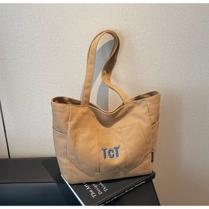 Macro detail of khaki canvas tote bag with blue embroidered TCT logo and side pocket