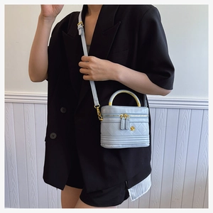 Detailed view of light blue quilted box bag with gold metal handle on black suit