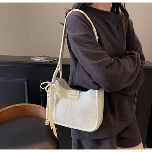 Detail of cream white bucket bag featuring lace bow and pearl charm strap accent