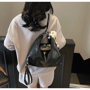 Detail of black glossy PU leather shoulder bag with white pom-pom charm on side