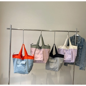 Detailed display of four color-blocked tote bags with front pockets on a metal hanger