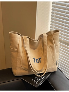 Large beige canvas tote bag with TCT blue embroidery on a black leather sofa
