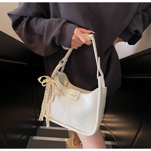 Detail of cream hobo bag with glossy pleated leather and pearl lace bow accessory