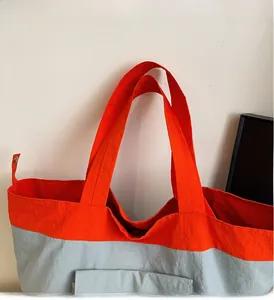 Detail view of the wide orange handles and side pocket on this casual grey tote bag