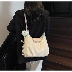 Detail view of cream tote bag featuring pink flap button closure and soft pompom charm