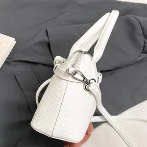 Detailed macro of silver metal hook and pebbled white leather on a crossbody handbag
