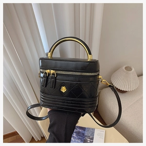 Macro detail of black quilted box bag featuring a unique gold curved handle and floral logo
