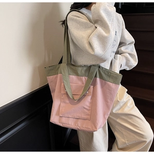 Detail of green and pink large tote bag with front pocket carried by a model