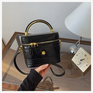 Detail of black quilted leather box bag with gold metal handle and camellia flower ornament
