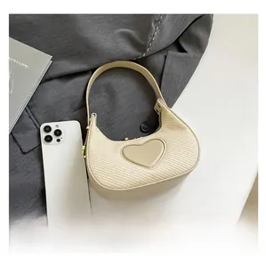 Detail der gewebten cremefarbenen Mondsichel-Tasche mit großem Herz-Patch auf dem Tisch