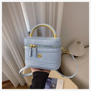 Detail of light blue box bag featuring quilted texture and elegant gold top handle