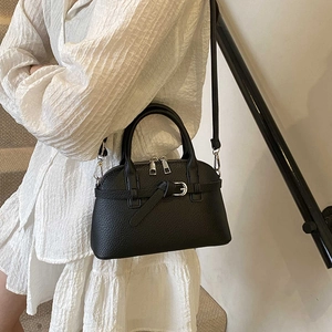 Detail of a black lychee-grain leather shell bag with silver hardware on a white dress