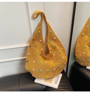 Detailed close-up of yellow crochet tote bag with colorful pearl beads on black leather sofa