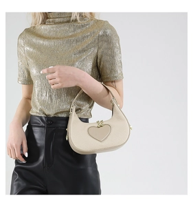 Detail der beigen halbmondförmigen Handtasche mit Herz-Patch und goldenen Kugel-Verschlüssen