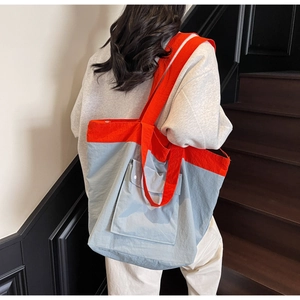 Detail of red straps on blue oversized tote bag with front pocket shown on shoulder