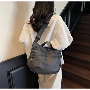 Detail of black nylon hobo bag showing adjustable strap and side brand label on model