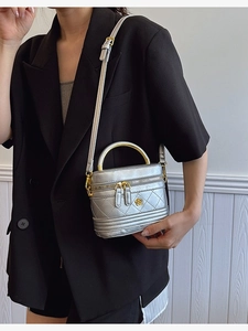 Silver quilted cylinder box bag with gold floral logo and metallic handle strap