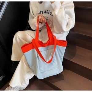 Detail of a large orange and blue tote bag featuring a front snap pocket on a model