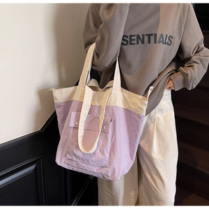 Detail of a purple and beige nylon tote bag with front snap pocket and wide strap handle