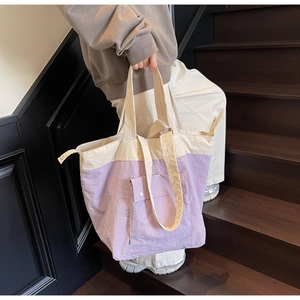 Detail of canvas tote bag with contrast stitching and front flap pocket on a wooden stair