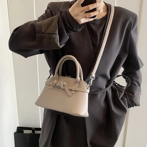 Beige pebble leather handbag with decorative knot detail worn as a crossbody bag