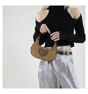 Detail of woven brown handbag featuring a leather heart patch and gold zipper hardware