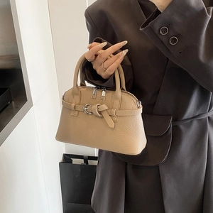 Close-up of beige lychee leather handbag with decorative belt buckle and silver zippers