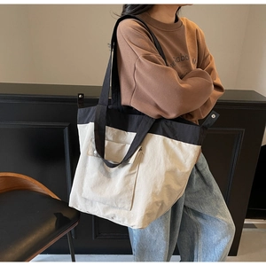 Close-up of a two-tone minimalist tote bag with a snap-button front pocket worn by a model