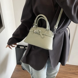 Detail of light green textured leather handbag with crossbody strap on a model